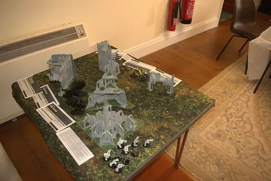 Battlefield setup for Warhammer game with miniatures and terrain pieces laid out on a table.