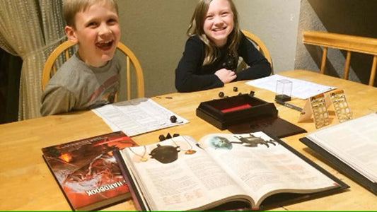 Two children smiling at a table set up for TTRPGs, showcasing the role of social interactions in gaming.
